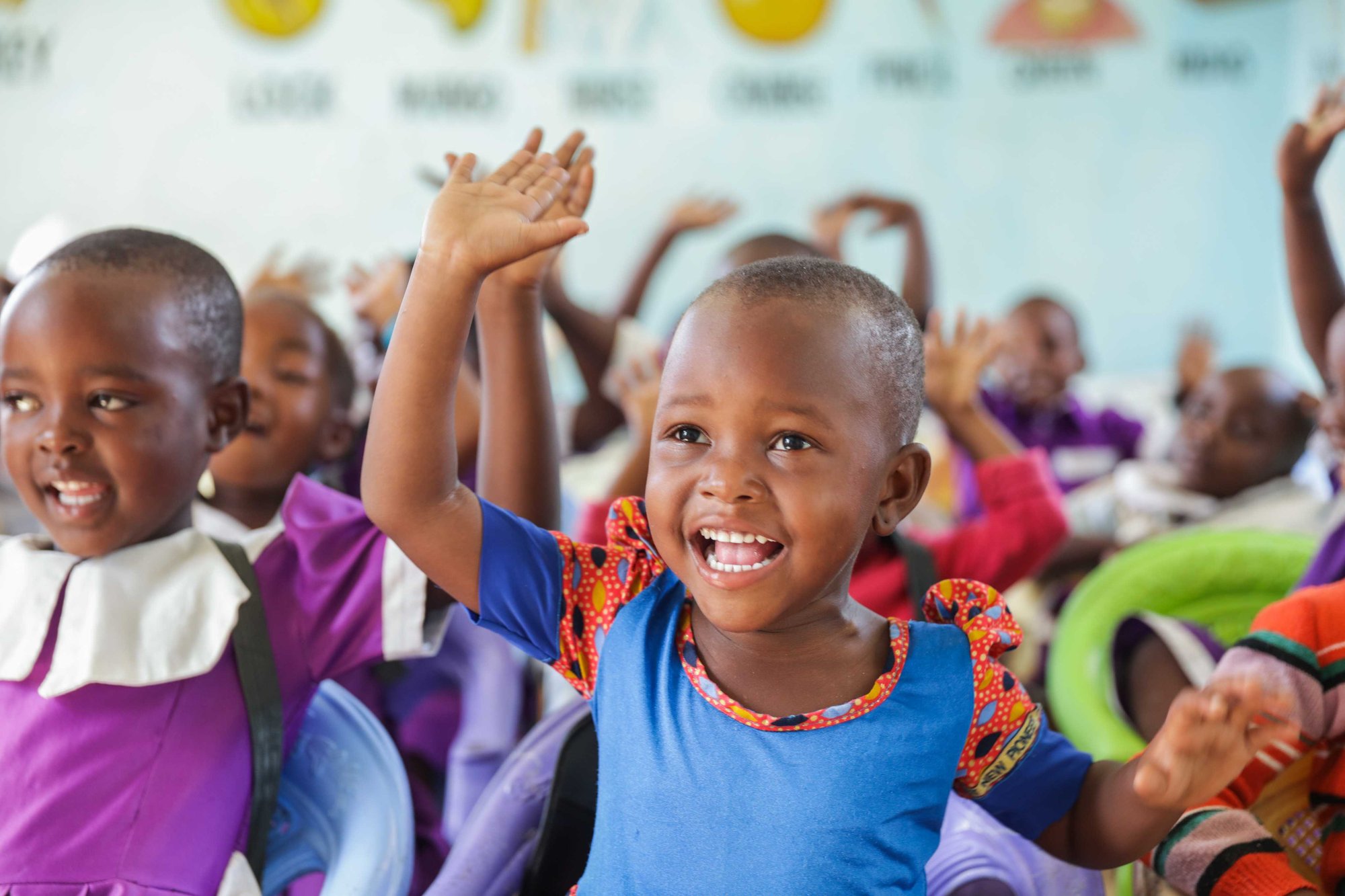 Jonge kinderen in Tanzania steken hun hand op in de klas.