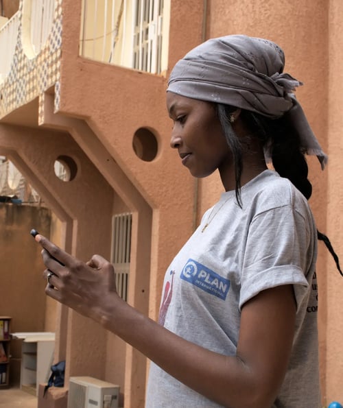 In Niger gebruikt Aïchatou, die een T-shirt met het logo van Plan International draagt, een online platform om een veilige omgeving te creëren voor de meisjes uit haar gemeenschap. 