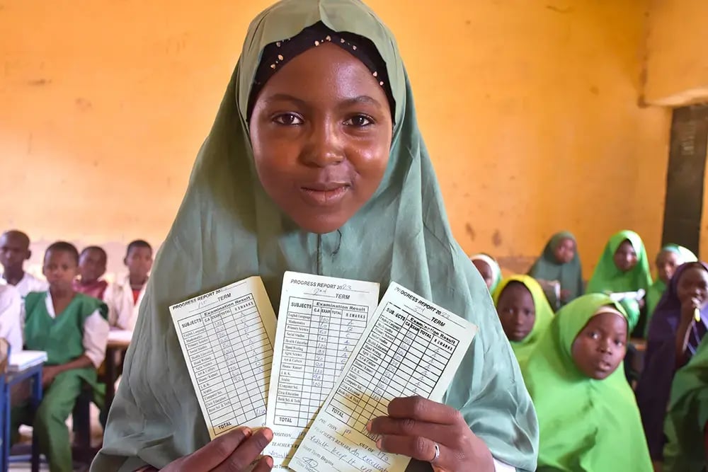 Aisha montre fièrement ses trois premiers bulletins scolaires qui montrent sa progression exceptionnelle.