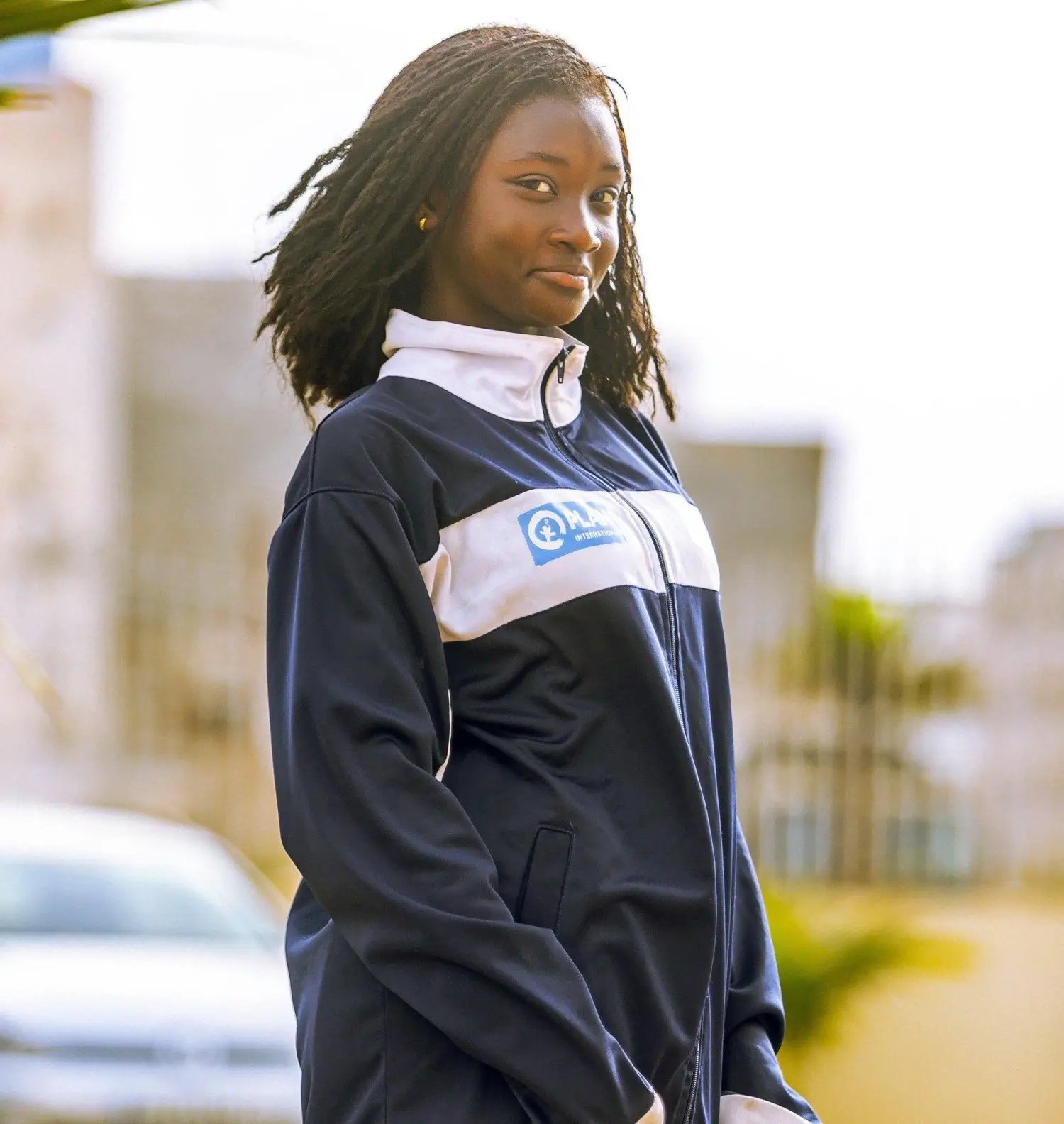 Aïda pose fièrement dans la rue avec une tenue arborant le logo de Plan International. 
