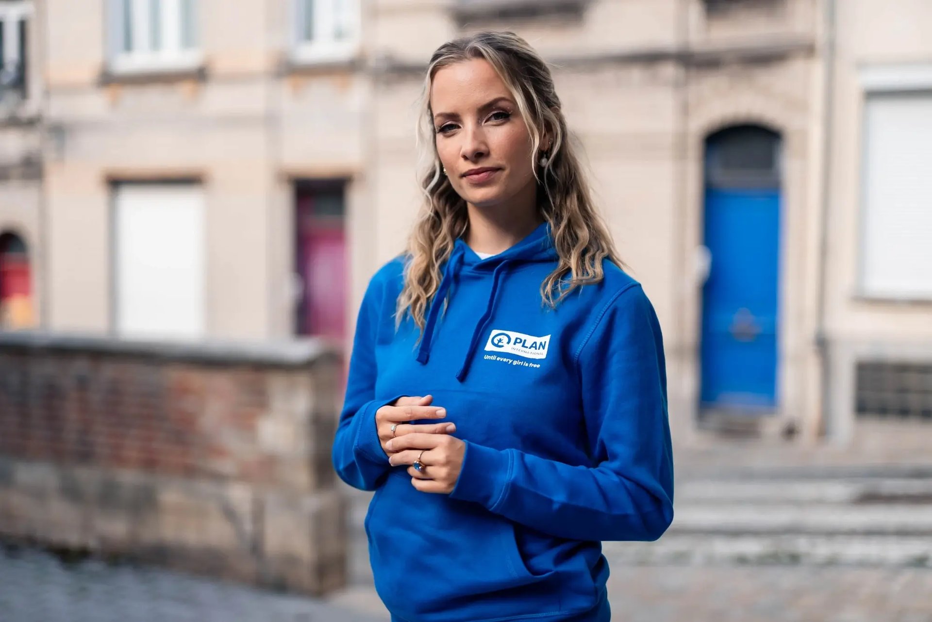 Olivia Trappeniers pose dans la rue avec un sweat à capuche bleu de Plan International Belgique