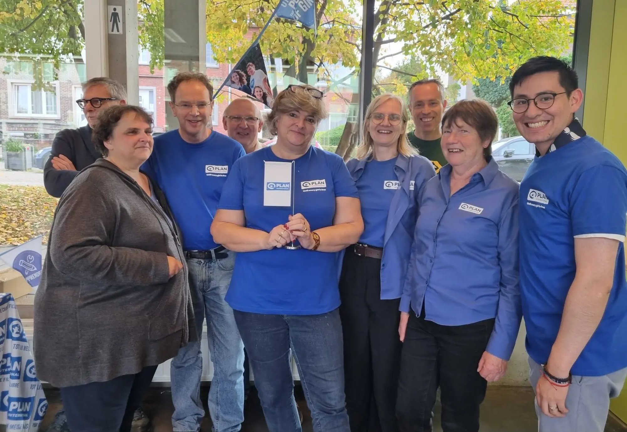 Een foto van de lokale werkgroep Antwerpen op hun jaarlijkse brunch.  Ze dragen allemaal hun blauwe Plan T-shirt en lachen breed naar de camera.