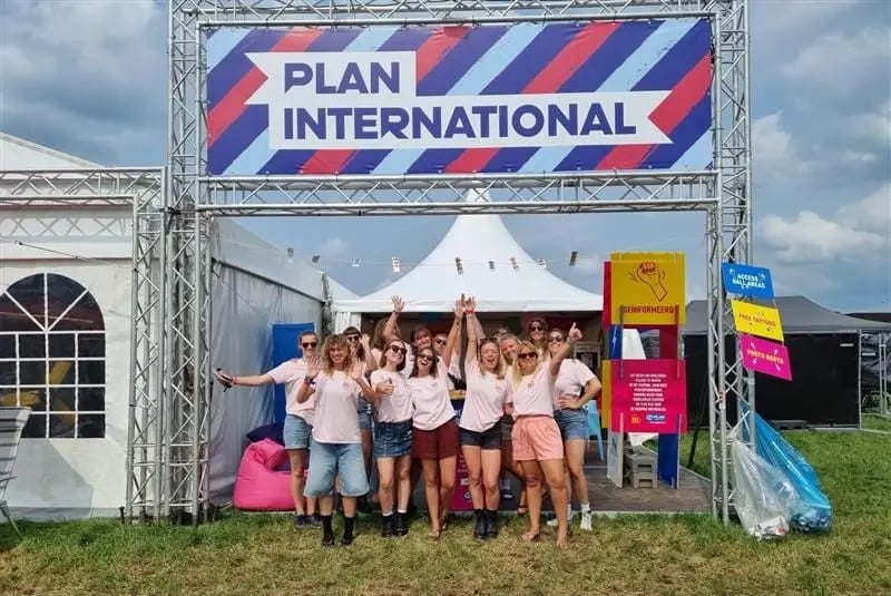 Groep enthousiaste vrijwilligers voor de stand op Pukkelpop. Ze dragen roze shirts en stralen samenhorigheid uit. 