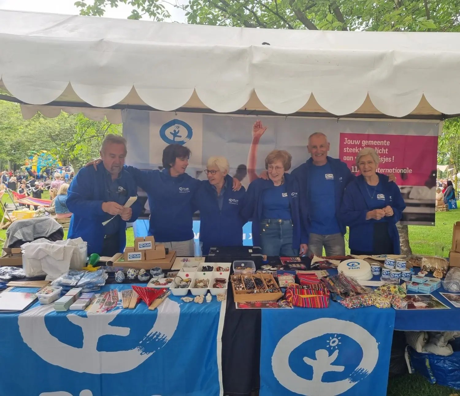 Op de foto zijn zes leden van de lokale werkgroep zichtbaar die achter hun blauwkleurige stand staan op Fiesta Mondial.