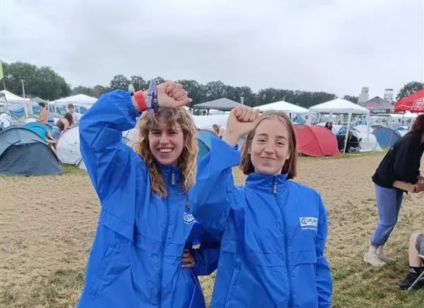 Deux volontaires, le poing levé, portant un imperméable bleu arborant le logo de Plan International Belgique