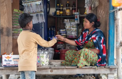 Ranju zit in haar winkeltje en verkoopt voedsel aan een kind 