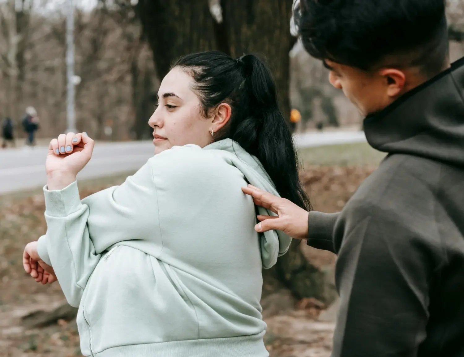 Une jeune femme s’étire dans un parc et un homme derrière elle lui touche le dos. 