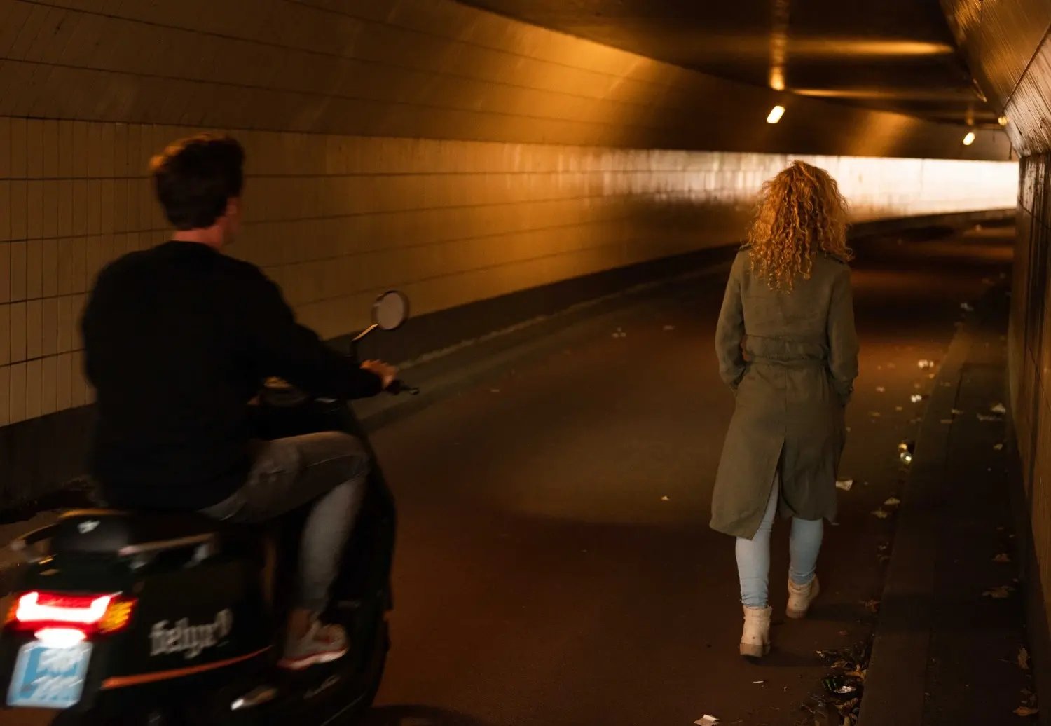 Een jonge vrouw (van achteren te zien) wandelt door een tunnel. Een man op een motorfiets passeert haar. (Plan International Nederland)