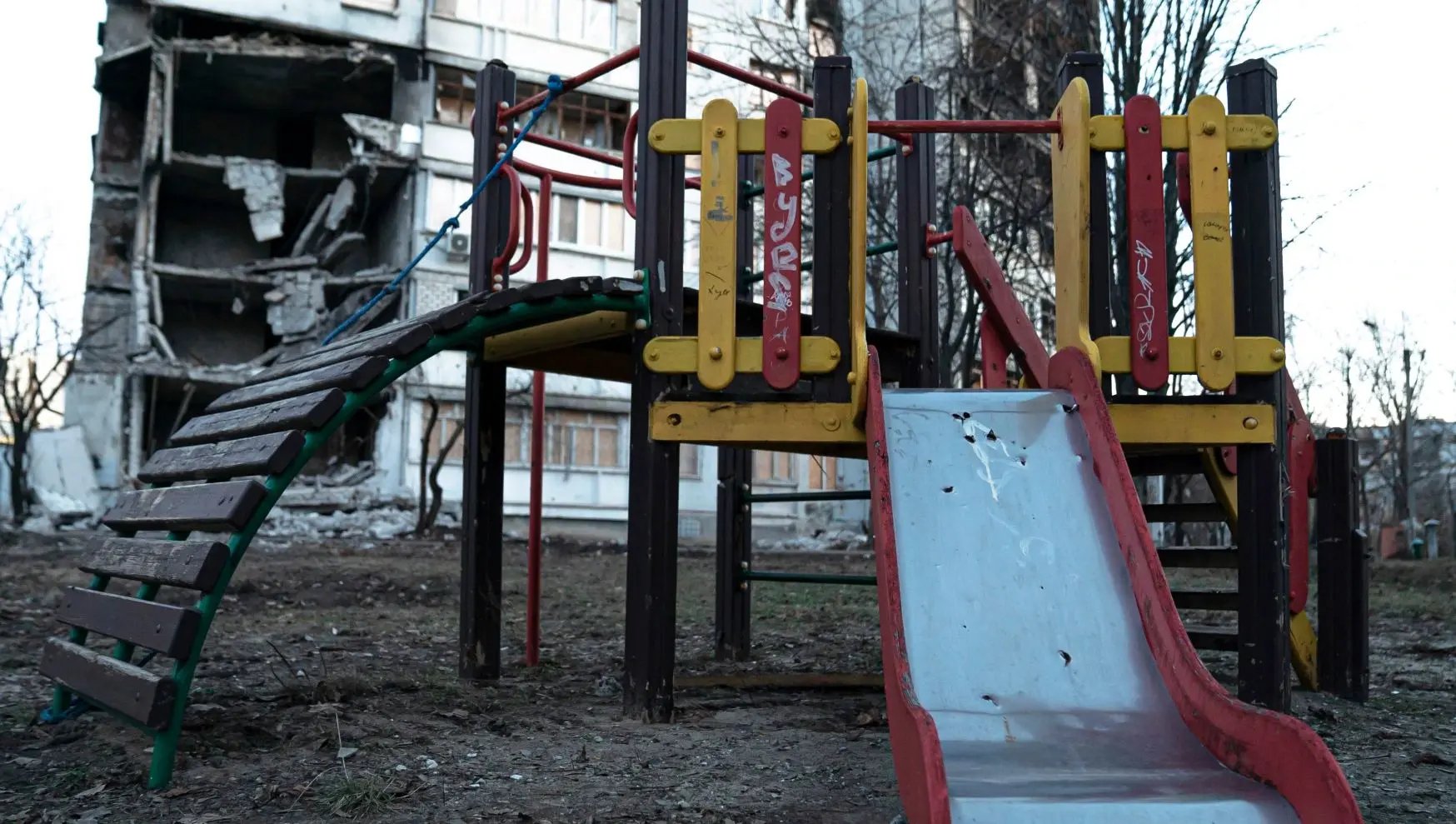 Une plaine de jeu vide devant un bâtiment partiellement démoli à cause du conflit en Ukraine.