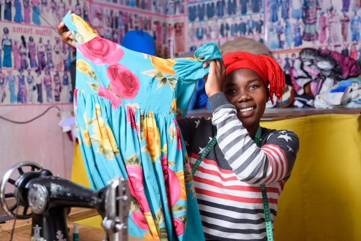 Een jonge vrouw in Tanzania laat trots een jurk zien die ze in haar naaiatelier heeft gemaakt