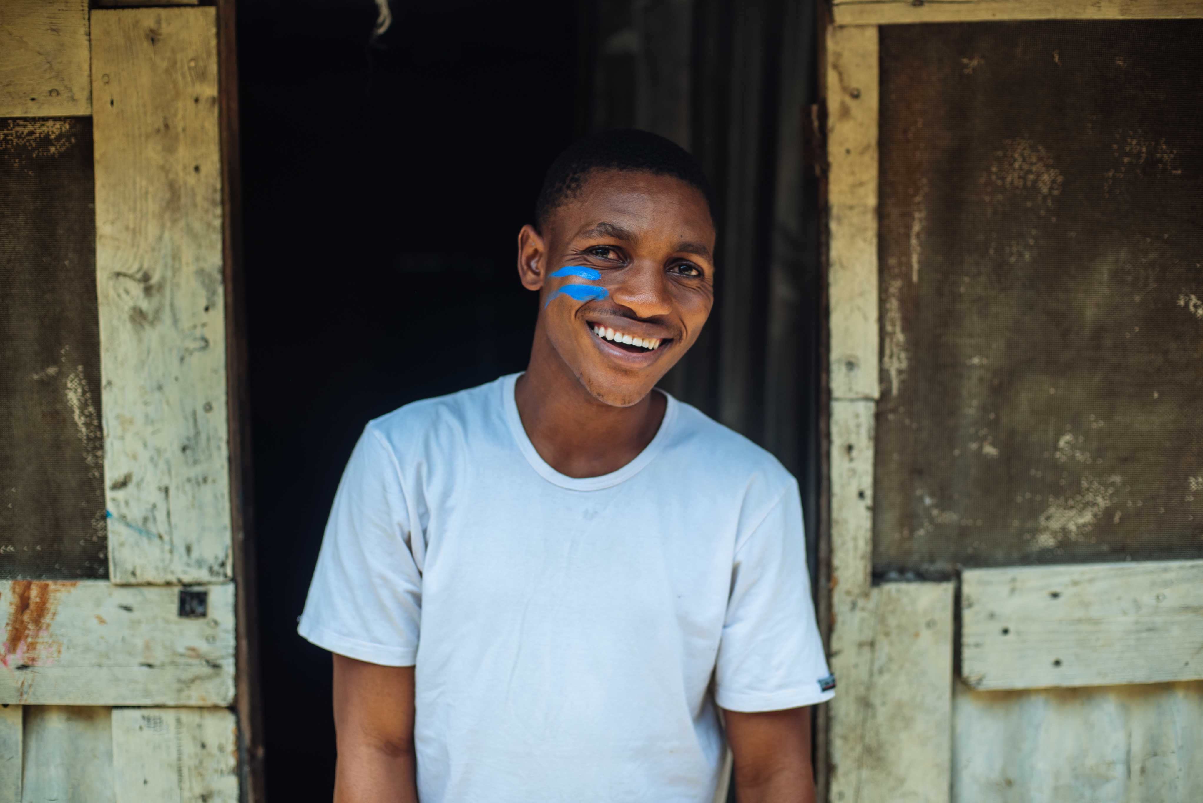 Anthony, 24 ans, sourit à la caméra. Il a des le symbole de l'égalité dessiné en bleu sur sa joue. Il fait partie de l'Alliance pour la défense des filles, un projet géré par Plan International.