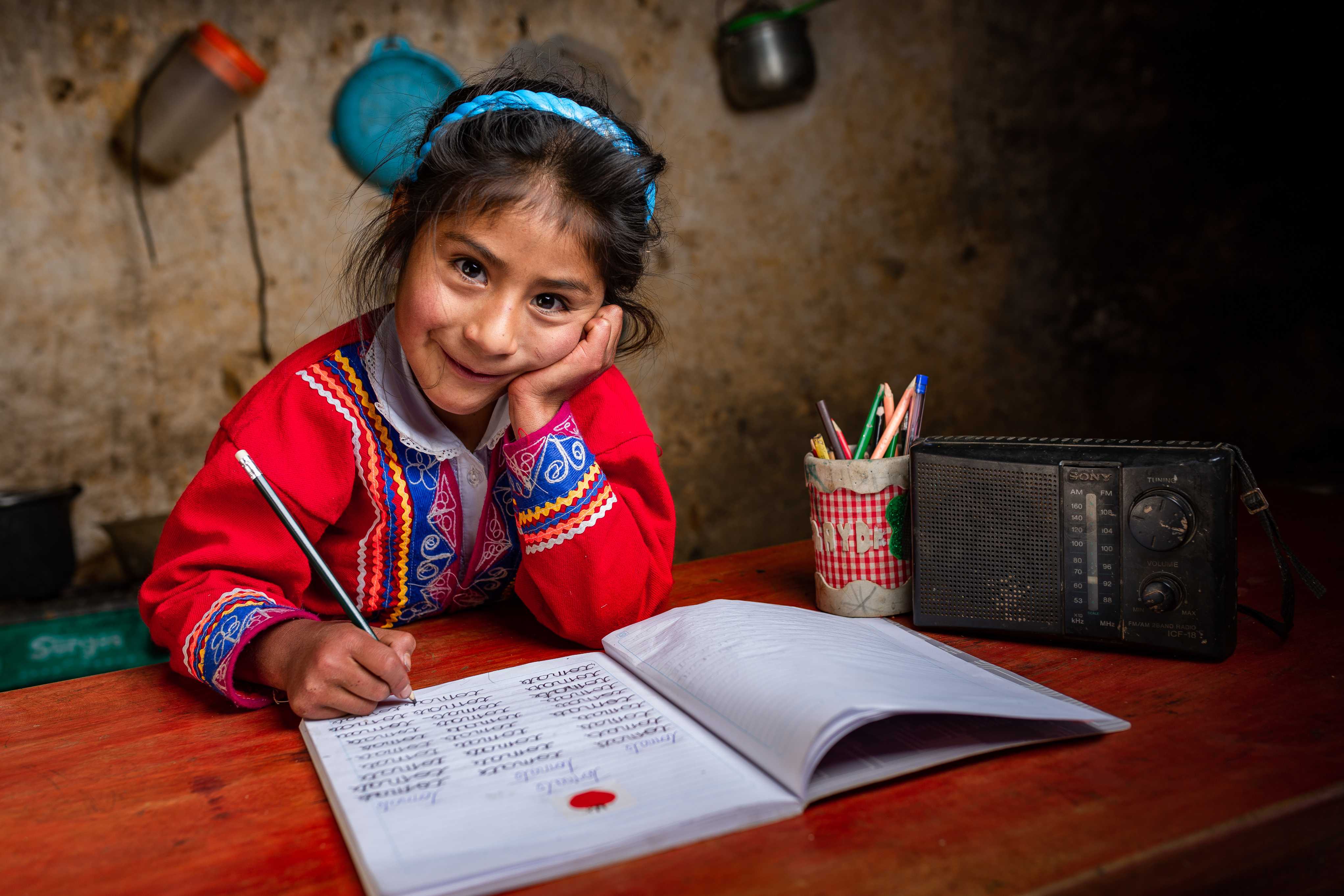 Een Peruaans schoolmeisje lacht voor de camera terwijl ze haar huiswerk maakt.