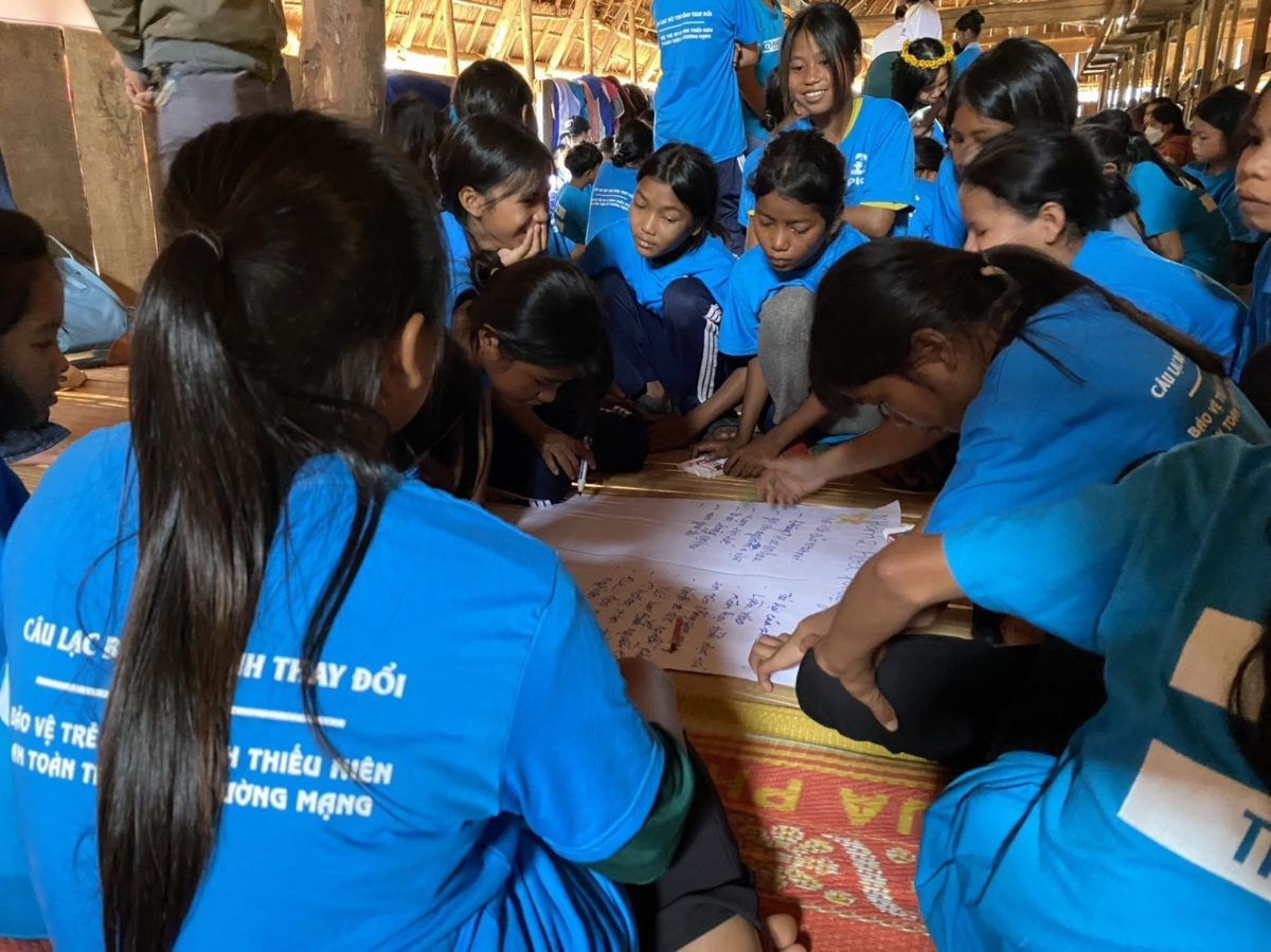 A group of girls each wearing a Plan International T-shirt sit around a sheet of paper on which they are working. This is a photo from our project in Vietnam. 