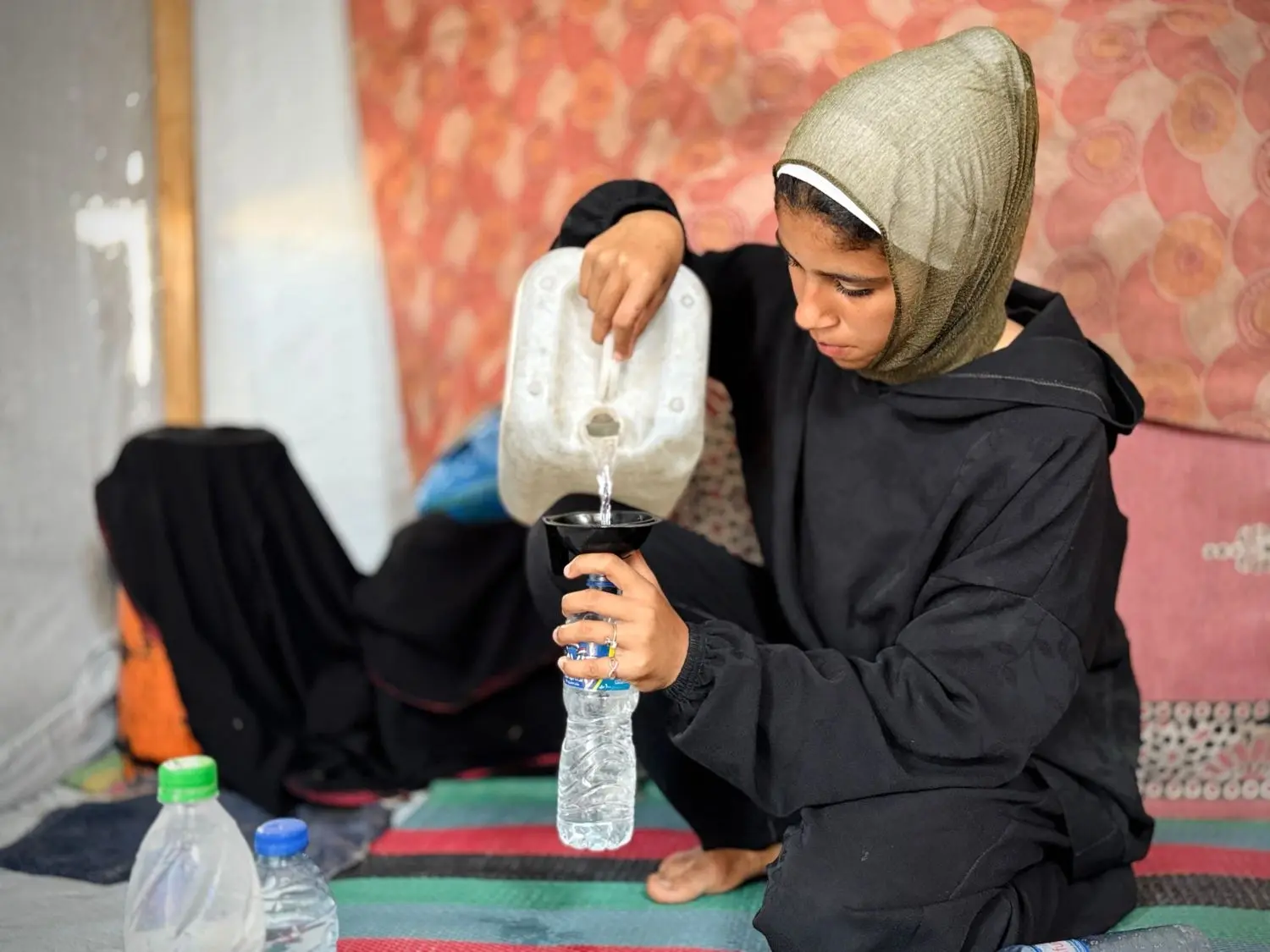 Une adolescente remplit d’eau des bouteilles en plastique à Gaza. © Plan International / Ahmed Salama