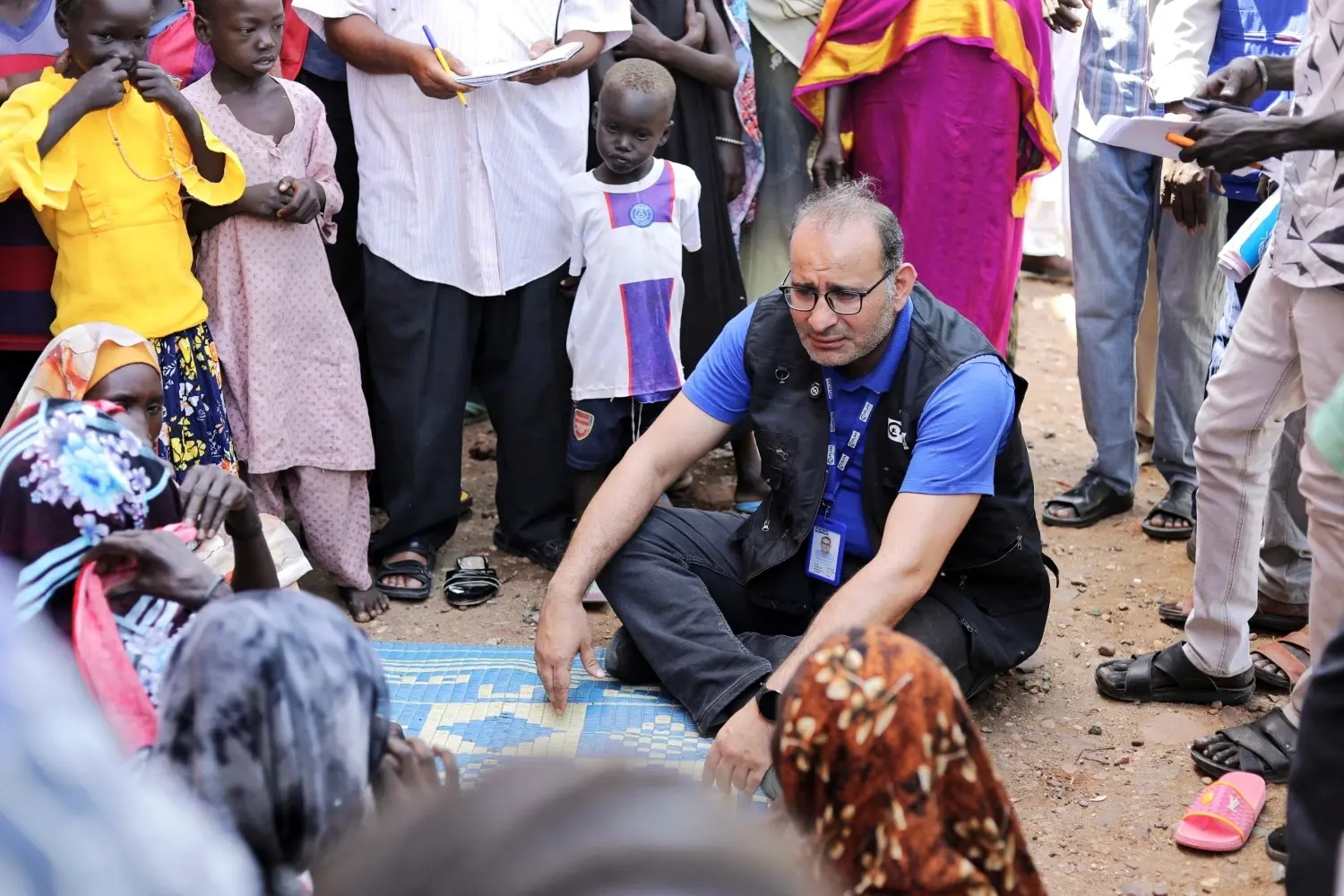 Mohamed Kamal, directeur national de Plan International Soudan, assis au milieu d’une foule au Soudan.