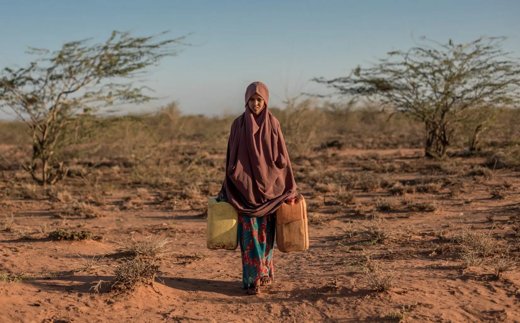 Une jeune fille de Somalie soulève des bidons d'eau. Sa vie est plus compliquée à cause de réchauffement climatique.