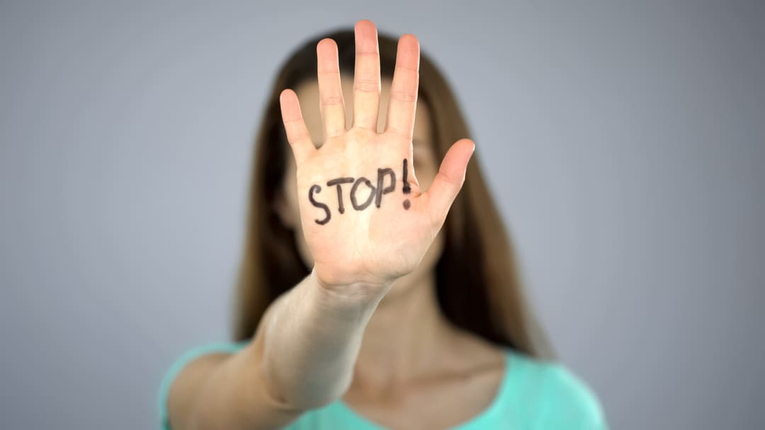 Jonge vrouw steekt haar rechterhand voor zich uit, met het woord 'STOP!' in zwart op haar handpalm geschreven 
